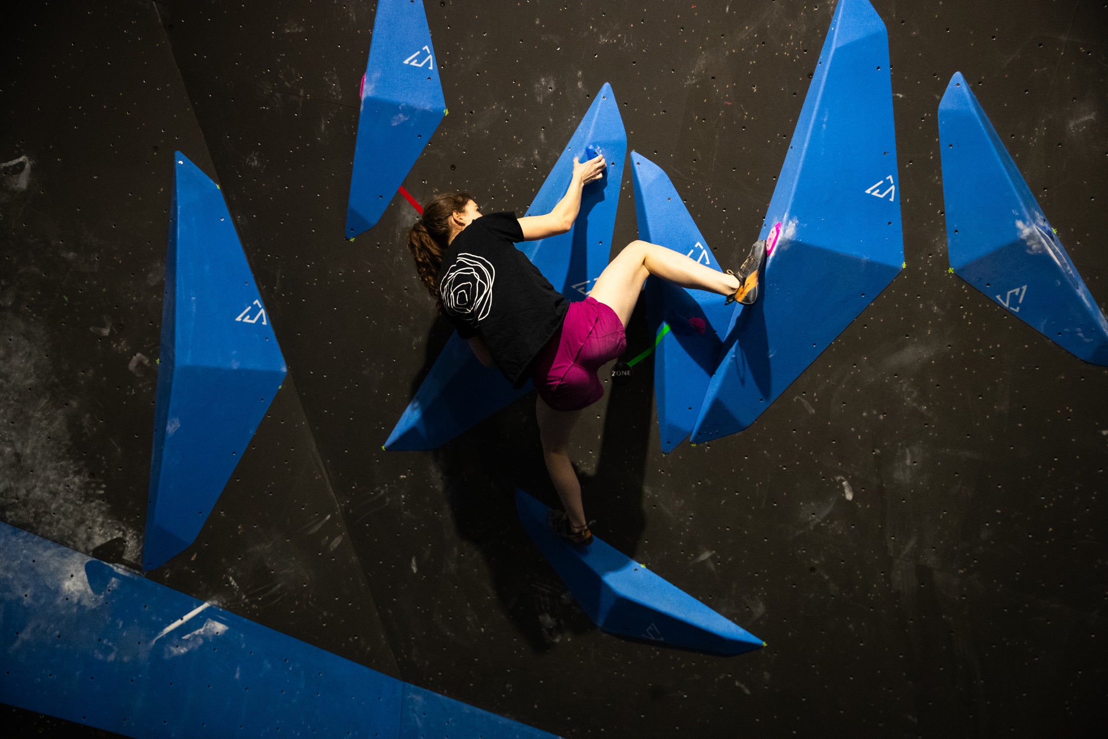 Athlete climbing on purple volumes beside a Solution Climbing banner at a competition